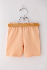 Dívčí šortky Lily Grey v jemné broskvové barvě zavěšené na dřevěném ramínku s kovovým hákem. Dívčí šortky Lily Grey v jemné broskvové barvě zavěšené na dřevěném ramínku s kovovým hákem.